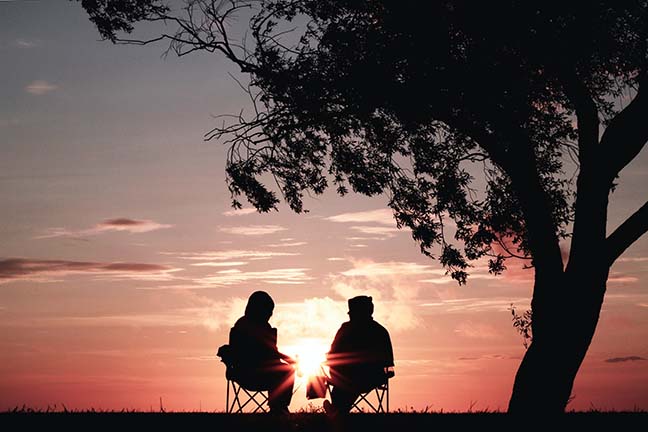 Couple Sitting together facing a Sunset